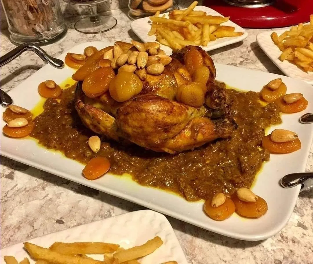 A whole roasted chicken with sauce, almonds and a side of fries