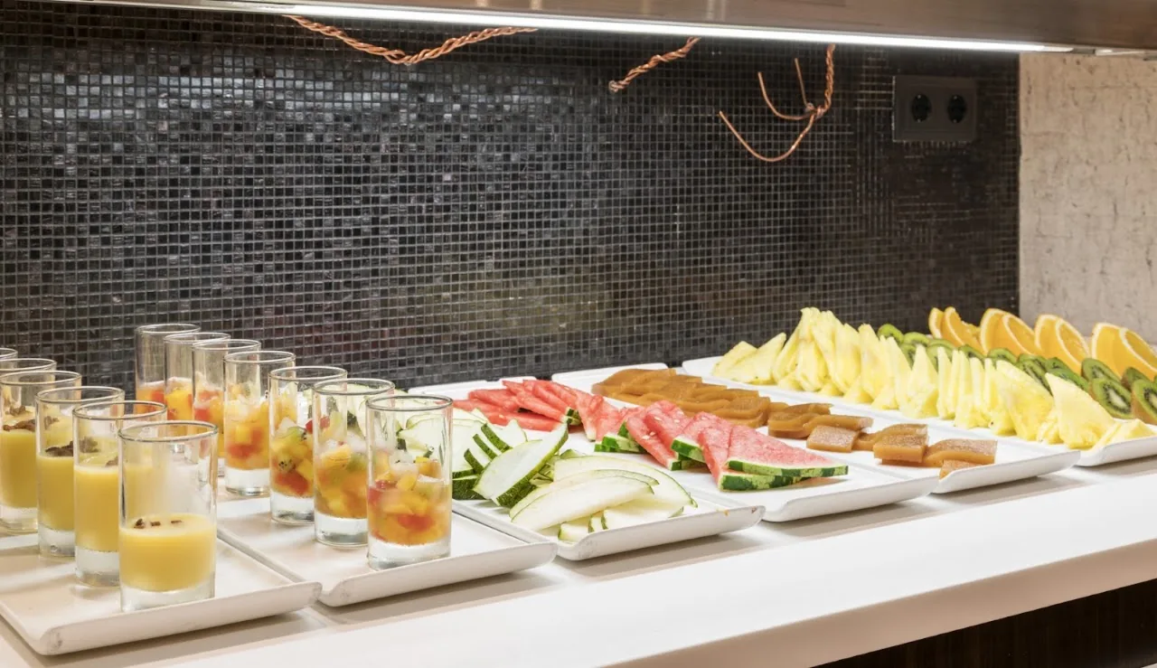 A hotel buffet spread of small dessert cups and a platter of sliced fruit