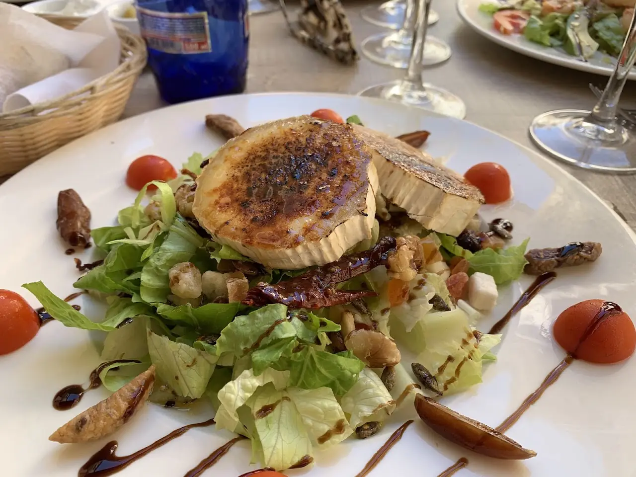 A seared round over a green salad with balsamic drizzle and cherry tomatoes