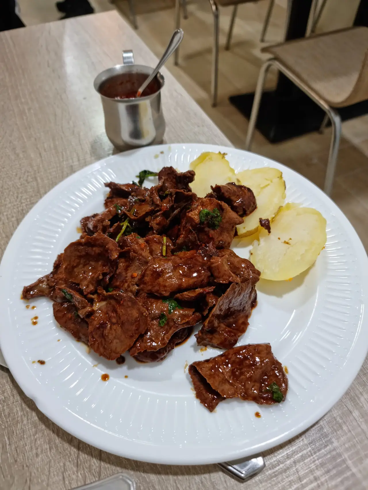 Plate of sliced stir-fried beef with boiled potato wedges and a side of hot sauce