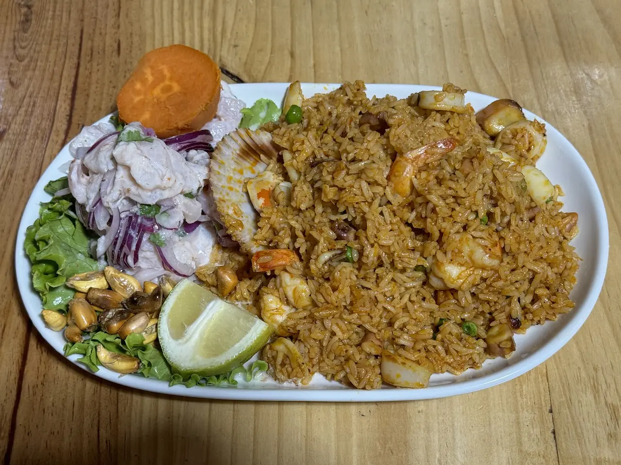 Platter of seafood fried rice with shrimp, squid and scallop, alongside a ceviche and lime wedge
