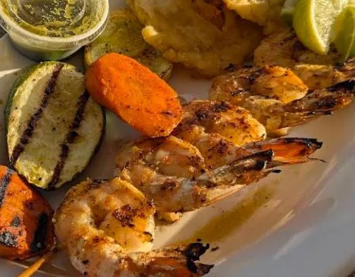 Grilled shrimp and vegetables on a plate with dipping sauces