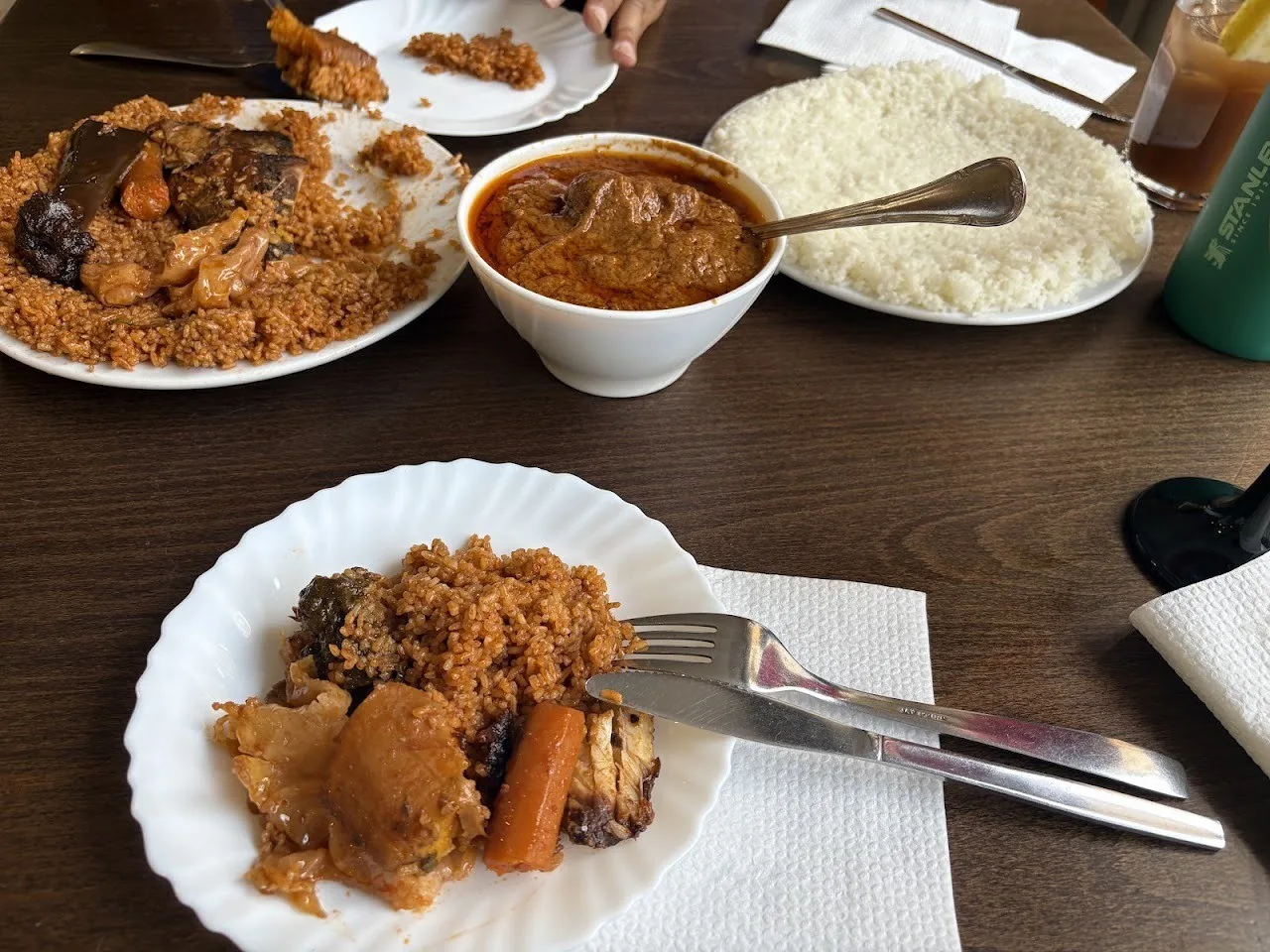 A table with plates of stew, rice and grains and a bowl of sauce