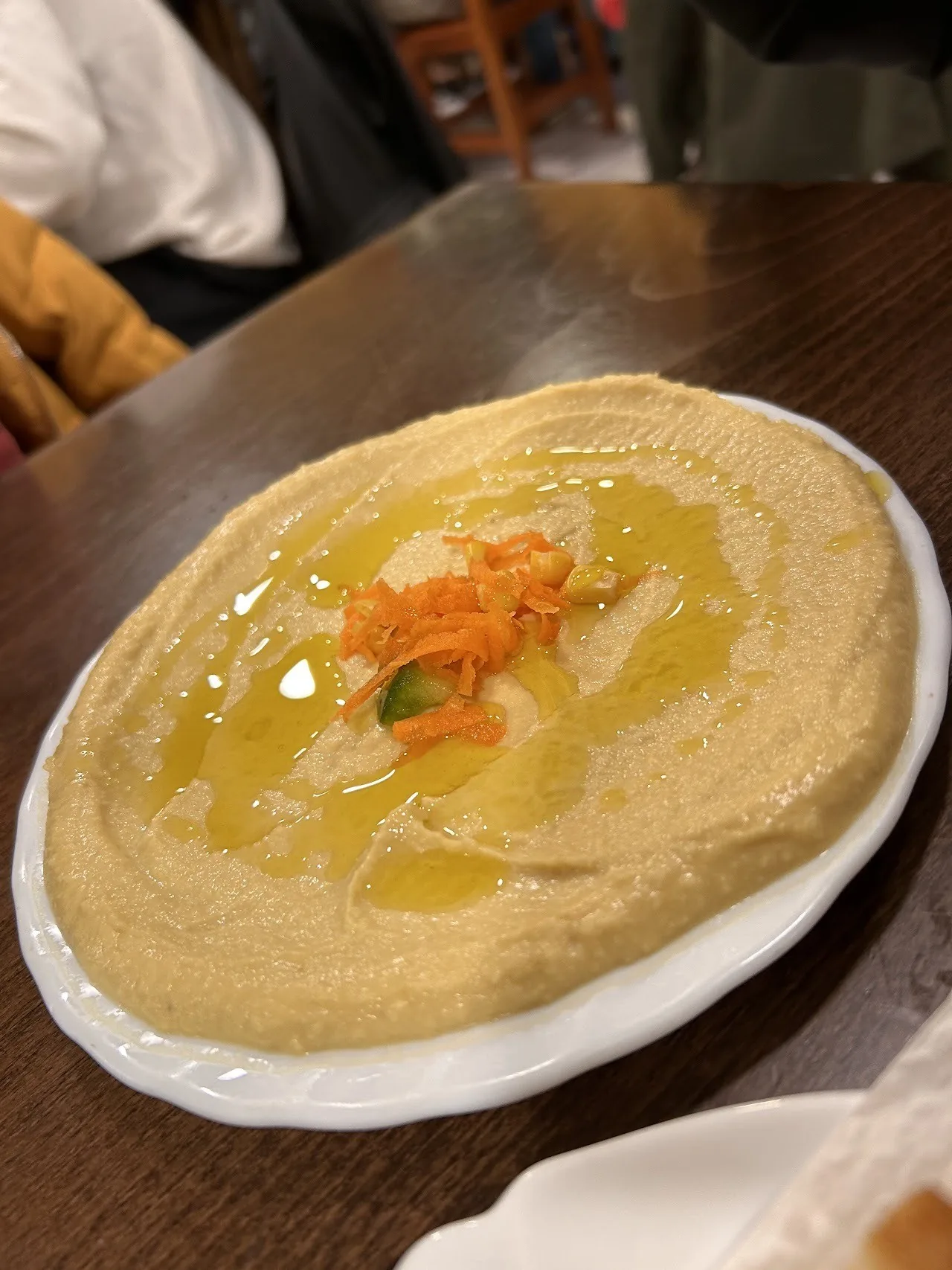 A plate of smooth hummus with olive oil and an orange topping