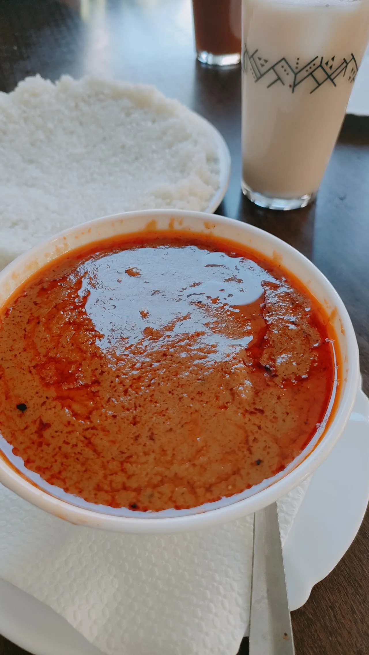 A bowl of orange-red spicy soup served in a paper cup