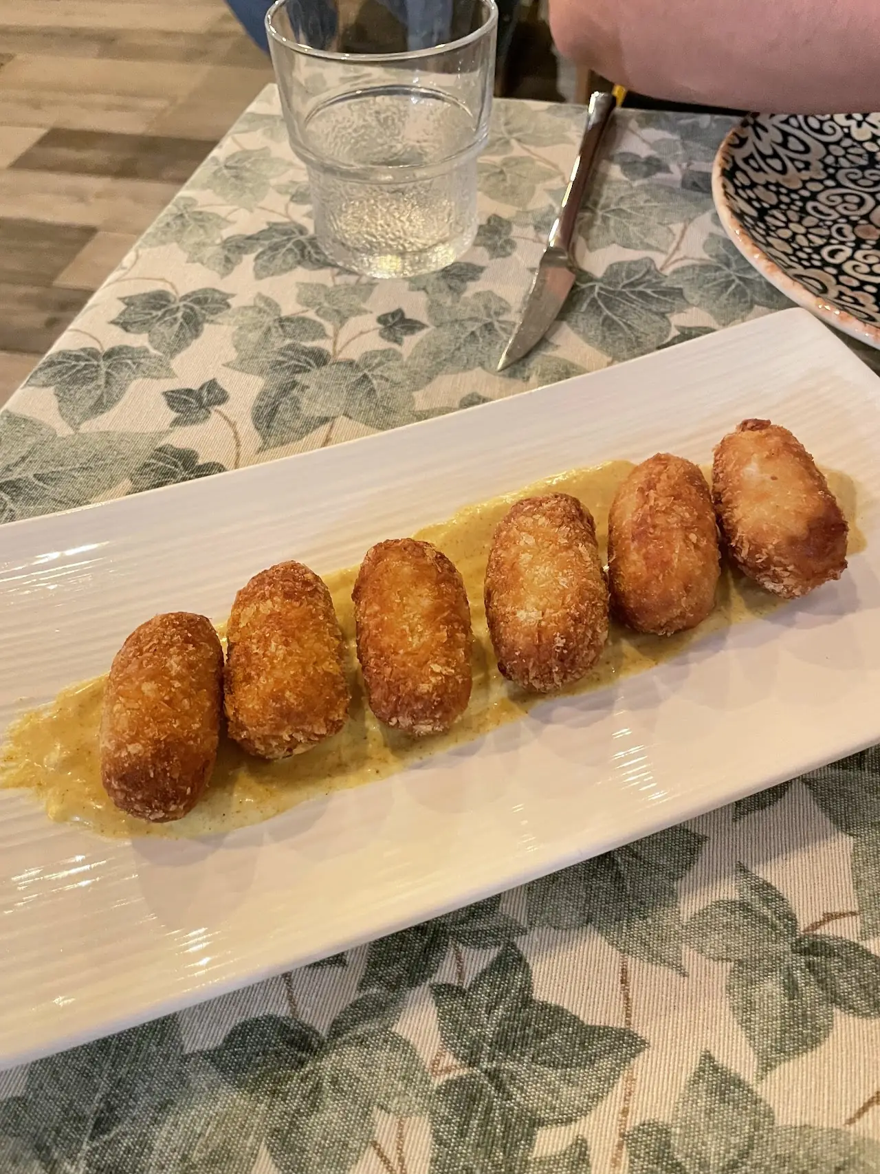 Breaded croquettes lined up on a rectangular plate with a light sauce.
