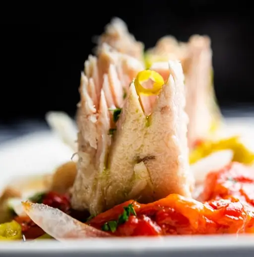 Flaked white fish served over roasted red peppers with a green oil drizzle on a white plate