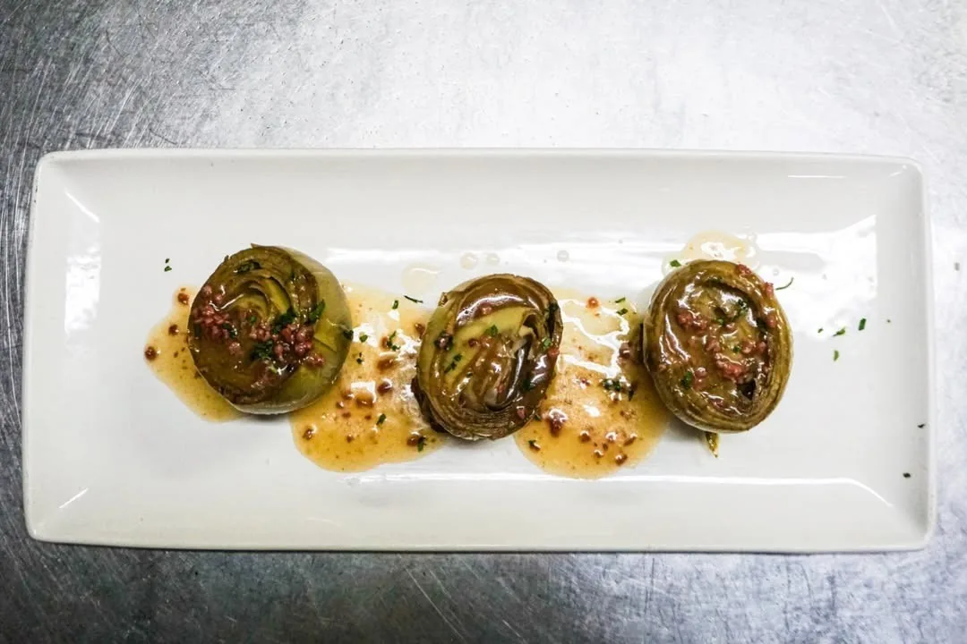 Three stuffed artichoke hearts in sauce on a white rectangular plate