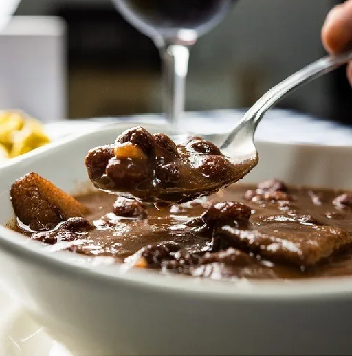 A spoon lifting dark beans and meat from a white bowl