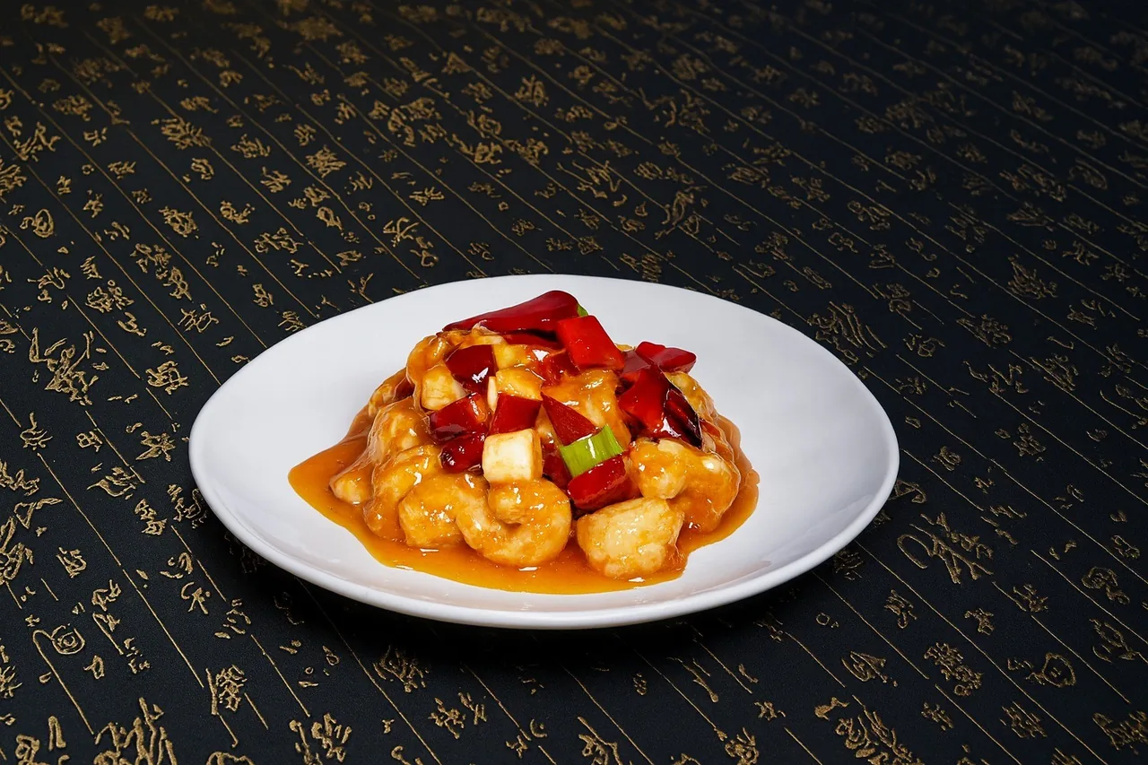 Prawns in an orange sauce with red peppers on a white plate