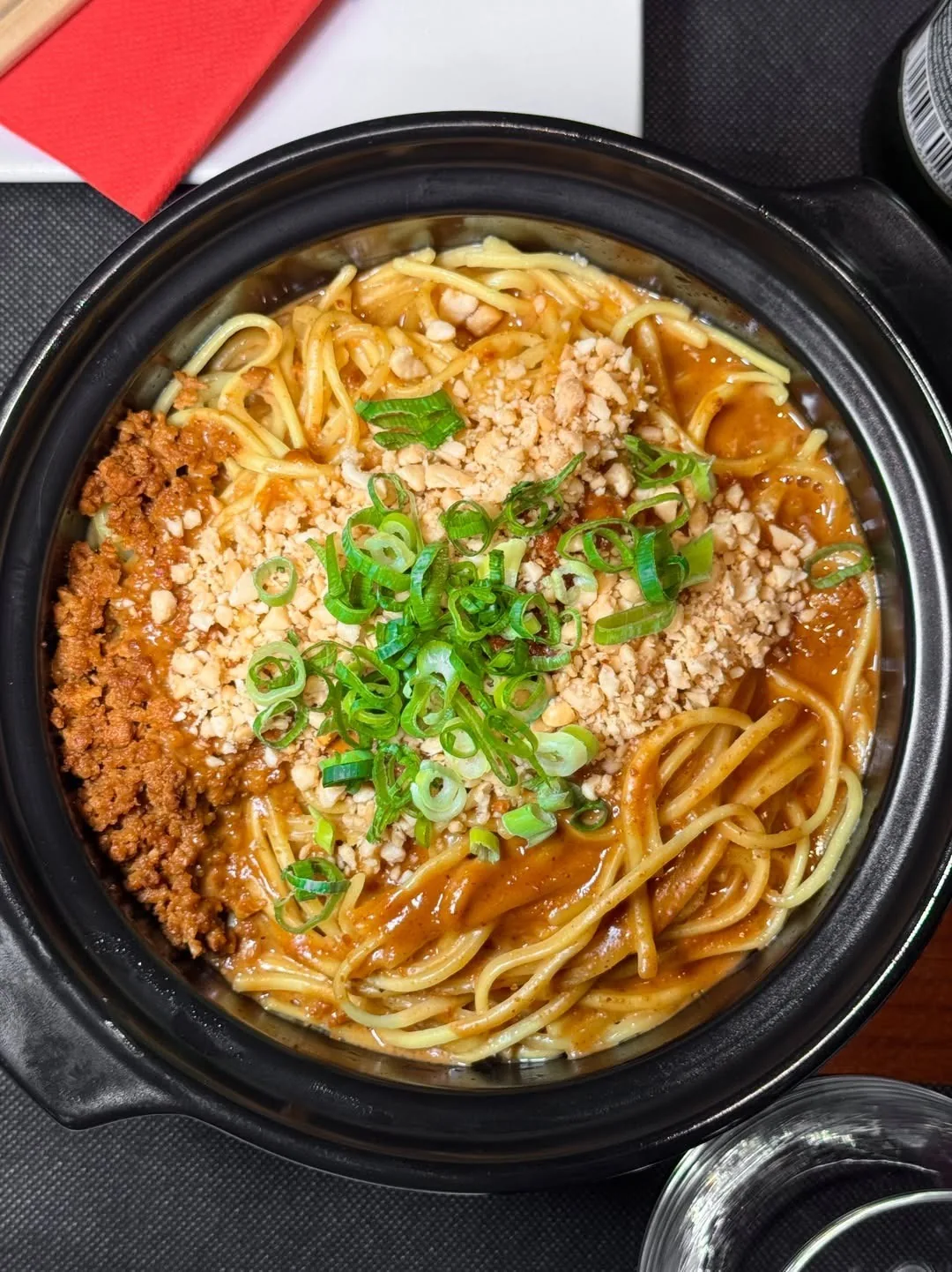 A black pot of noodles topped with minced meat and spring onion