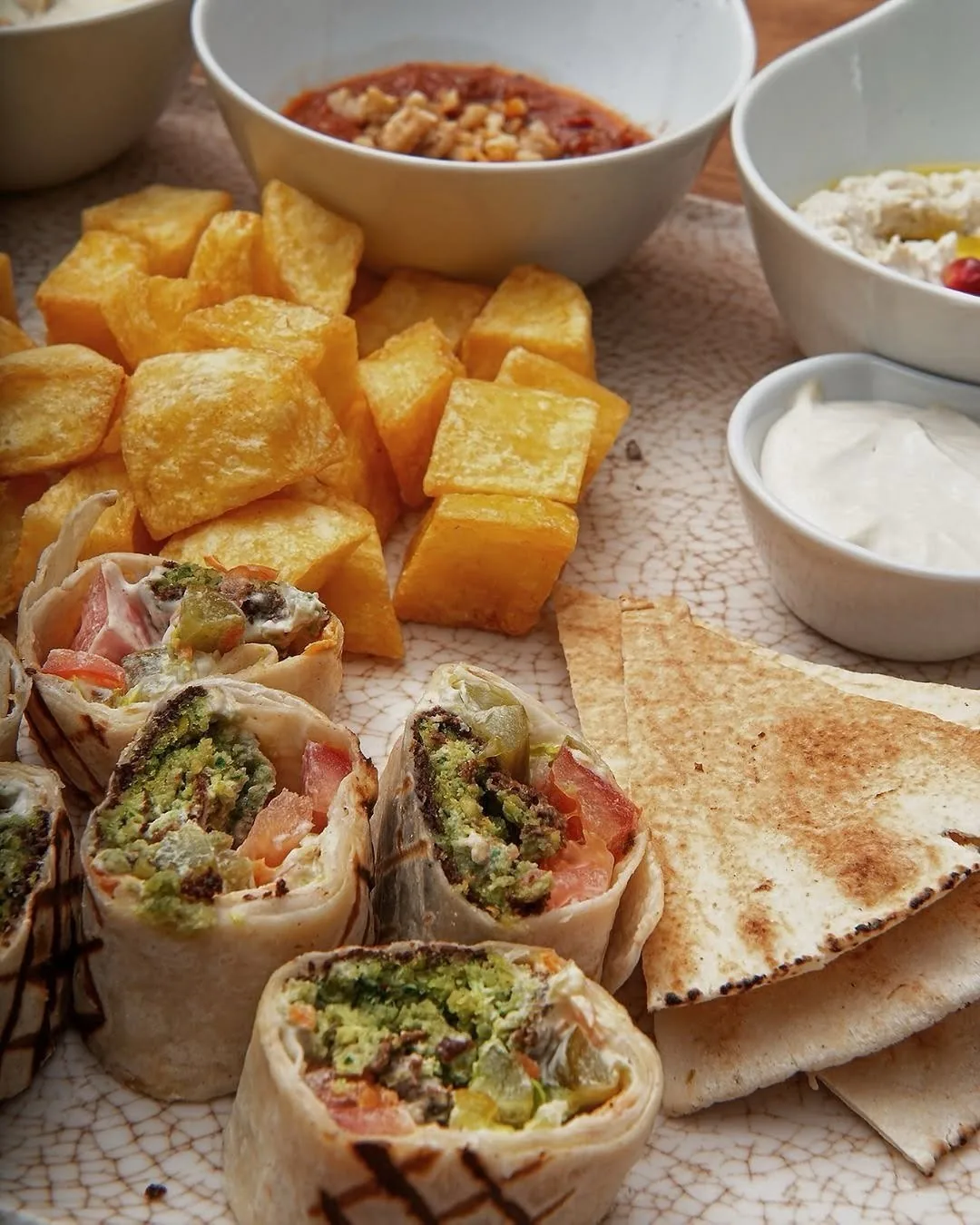 Wrapped flatbread sandwiches cut in halves next to fried potato cubes and pita triangles