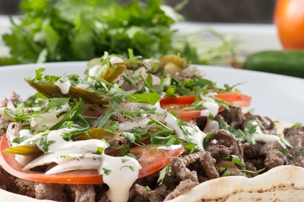 A plate of shredded meat over salad with tomatoes and a yogurt sauce