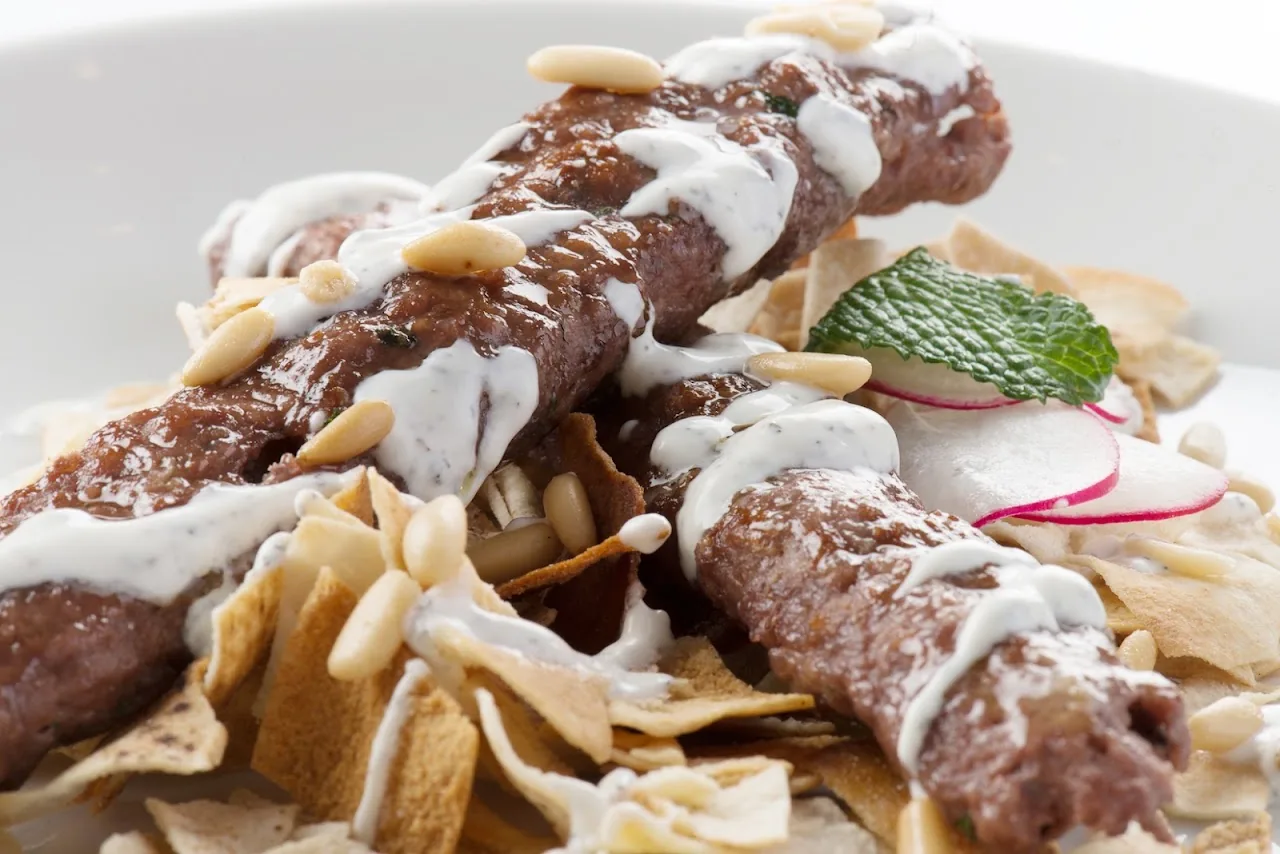 Grilled kofta skewers drizzled with garlic sauce and toasted almonds