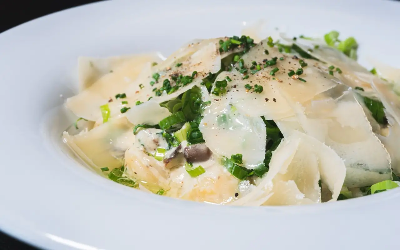 Creamy pasta with shaved parmesan, spring onion, chives, mushrooms and cracked pepper in a white bowl