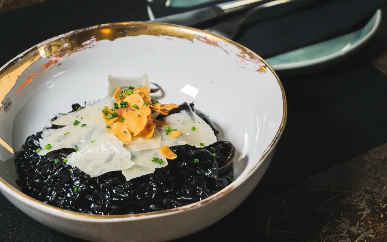 Squid-ink black rice topped with shaved cheese, fried garlic chips and chives in a gold-rimmed bowl