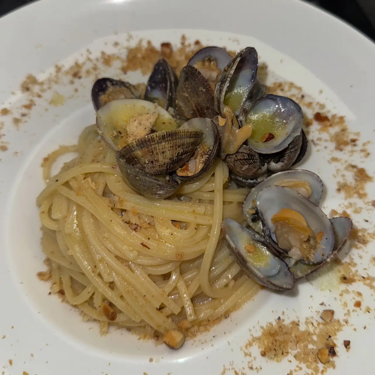 Spaghetti with clams in white wine sauce, topped with toasted breadcrumbs, on a white plate at Ristorante Capu