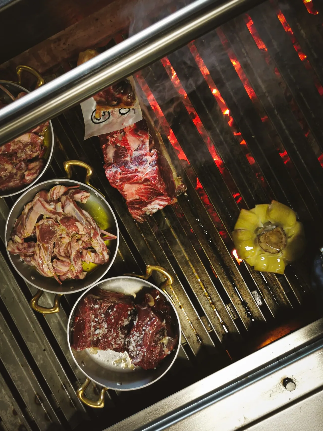 Meats and vegetables cooking in pans over a charcoal grill