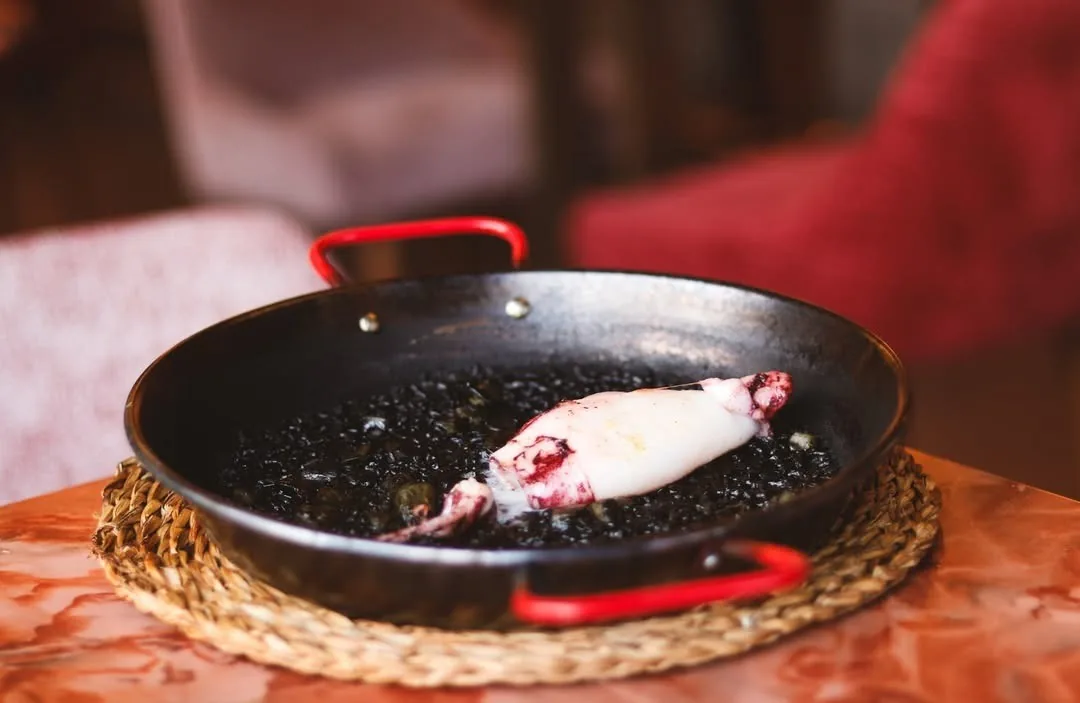 Black rice in a red-handled paella pan topped with a whole grilled squid