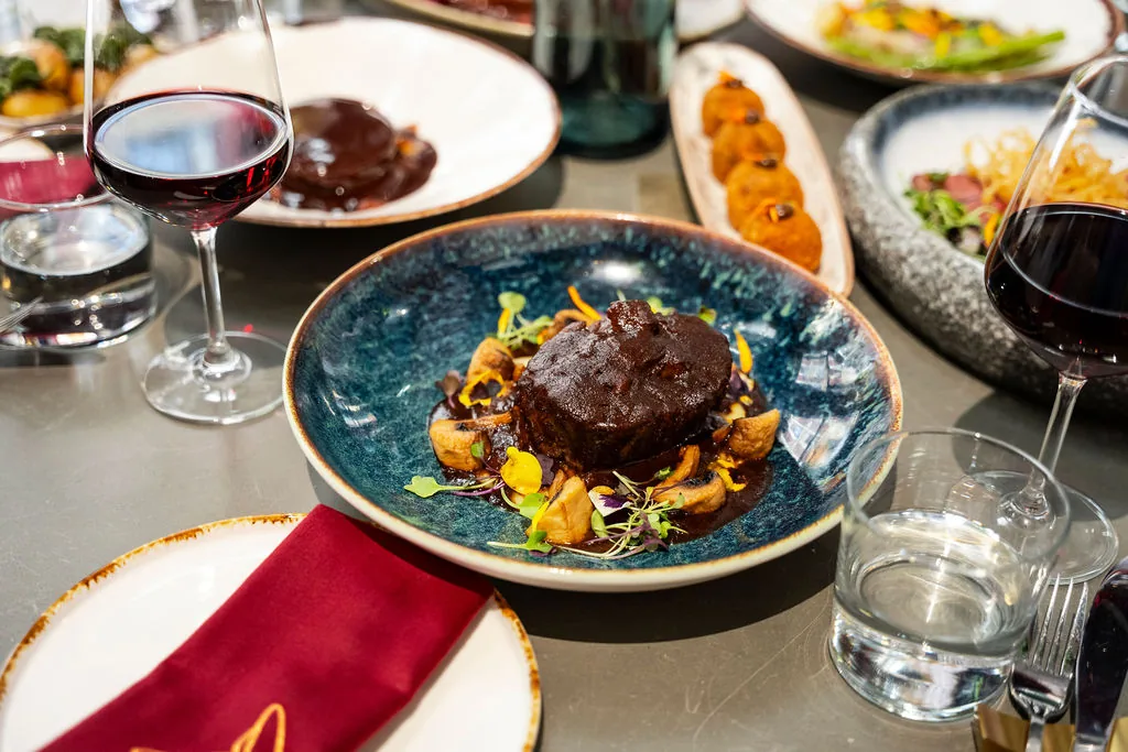 A plated dish of sliced meat with charred vegetables on a dark blue plate, set at the table