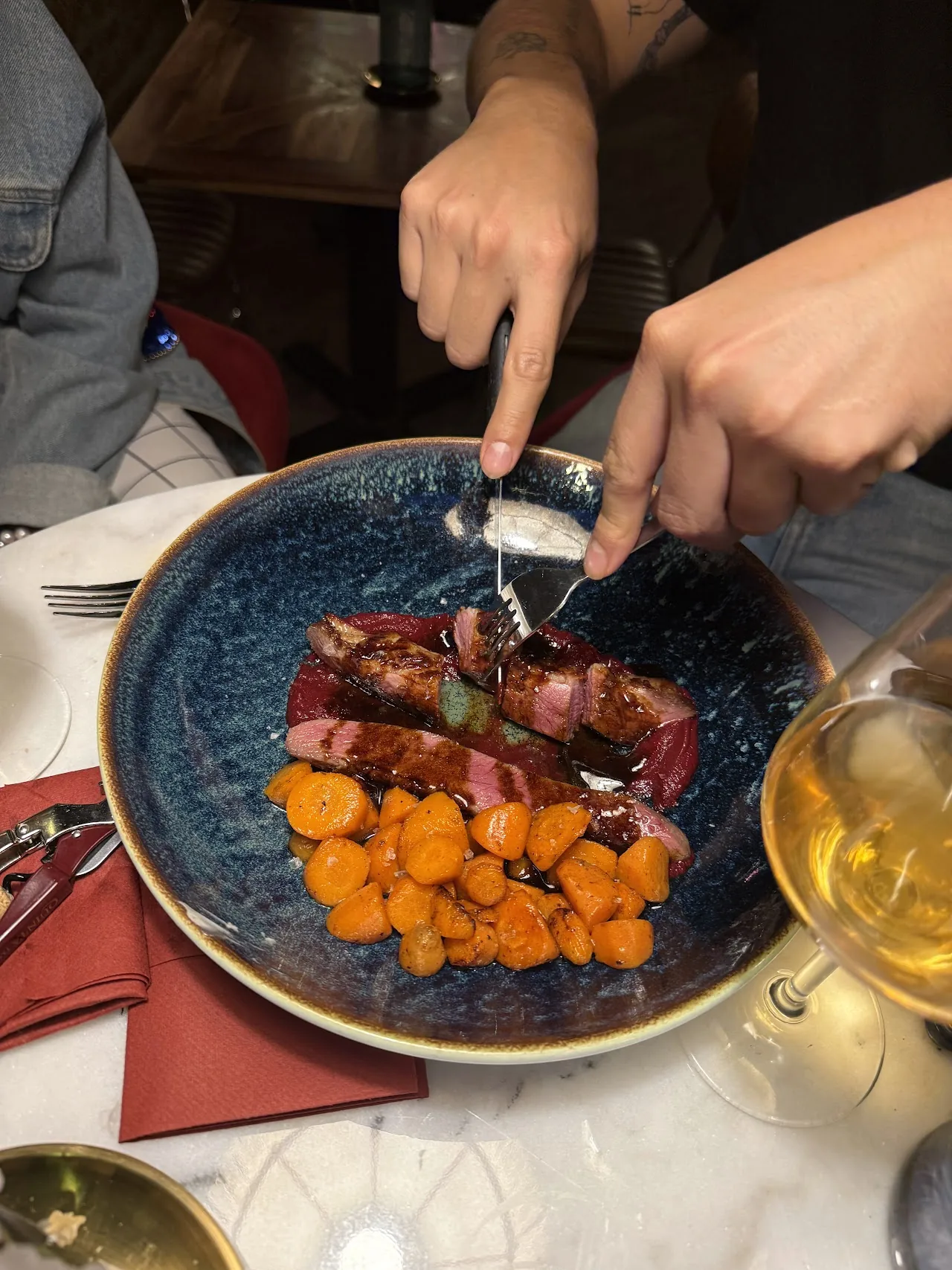 A diner cutting into a plate of meat with roasted orange vegetables