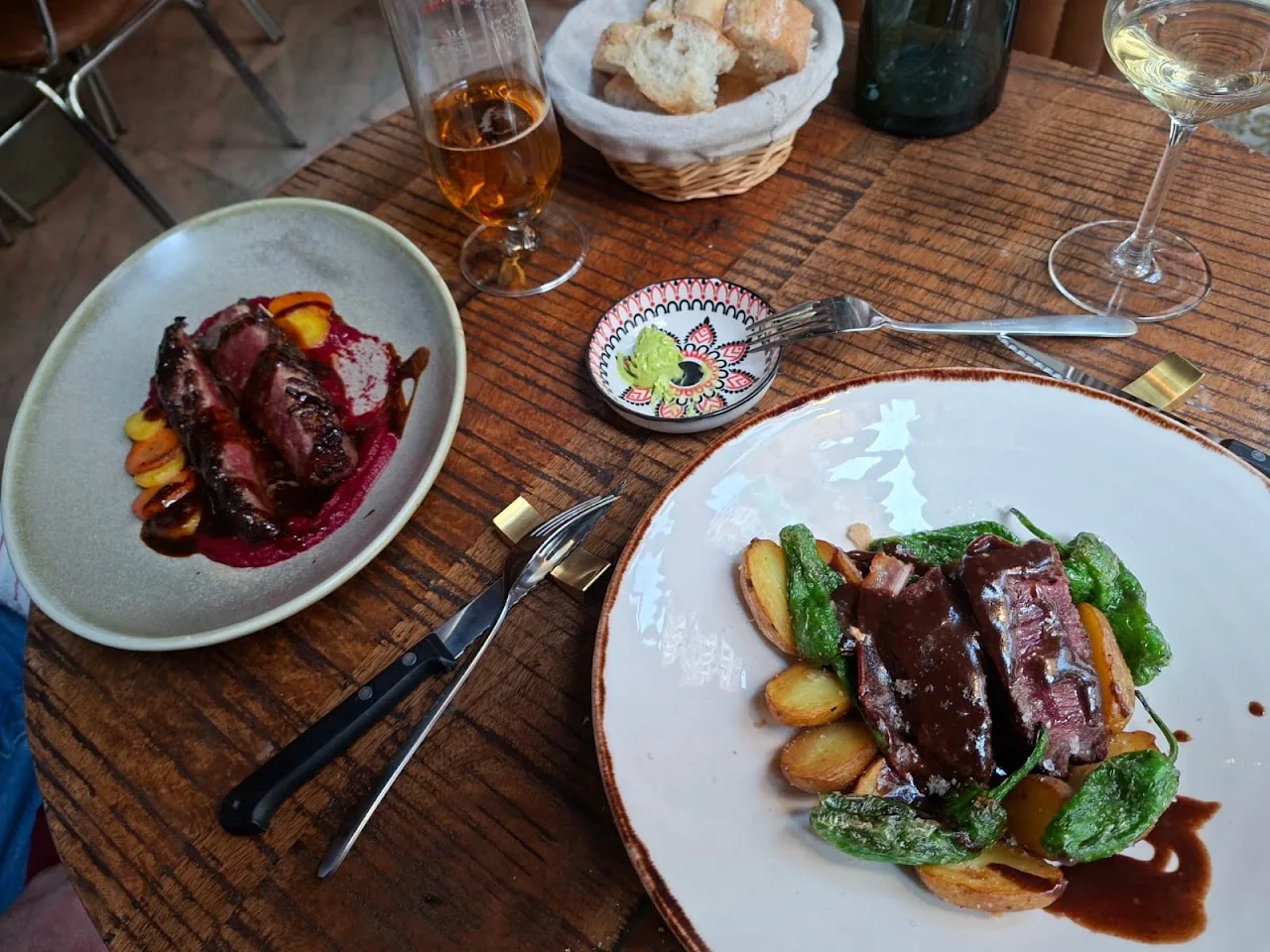 Two plates of food including sliced meat with dark sauce and roasted vegetables, with bread