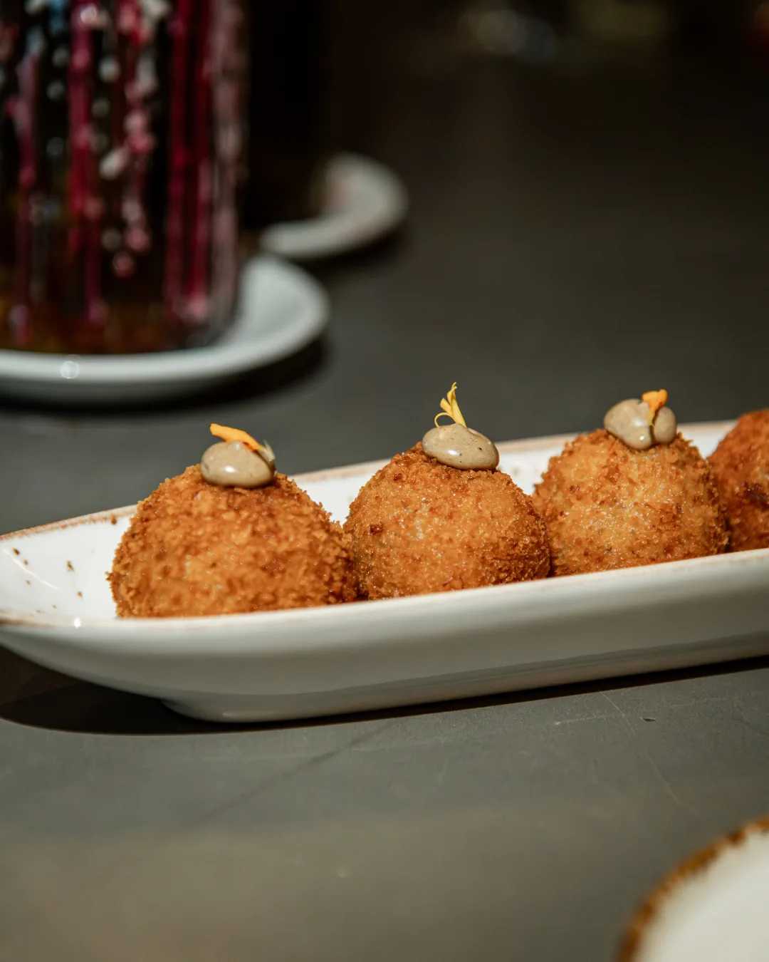 A plate of breaded croquettes drizzled with sauce