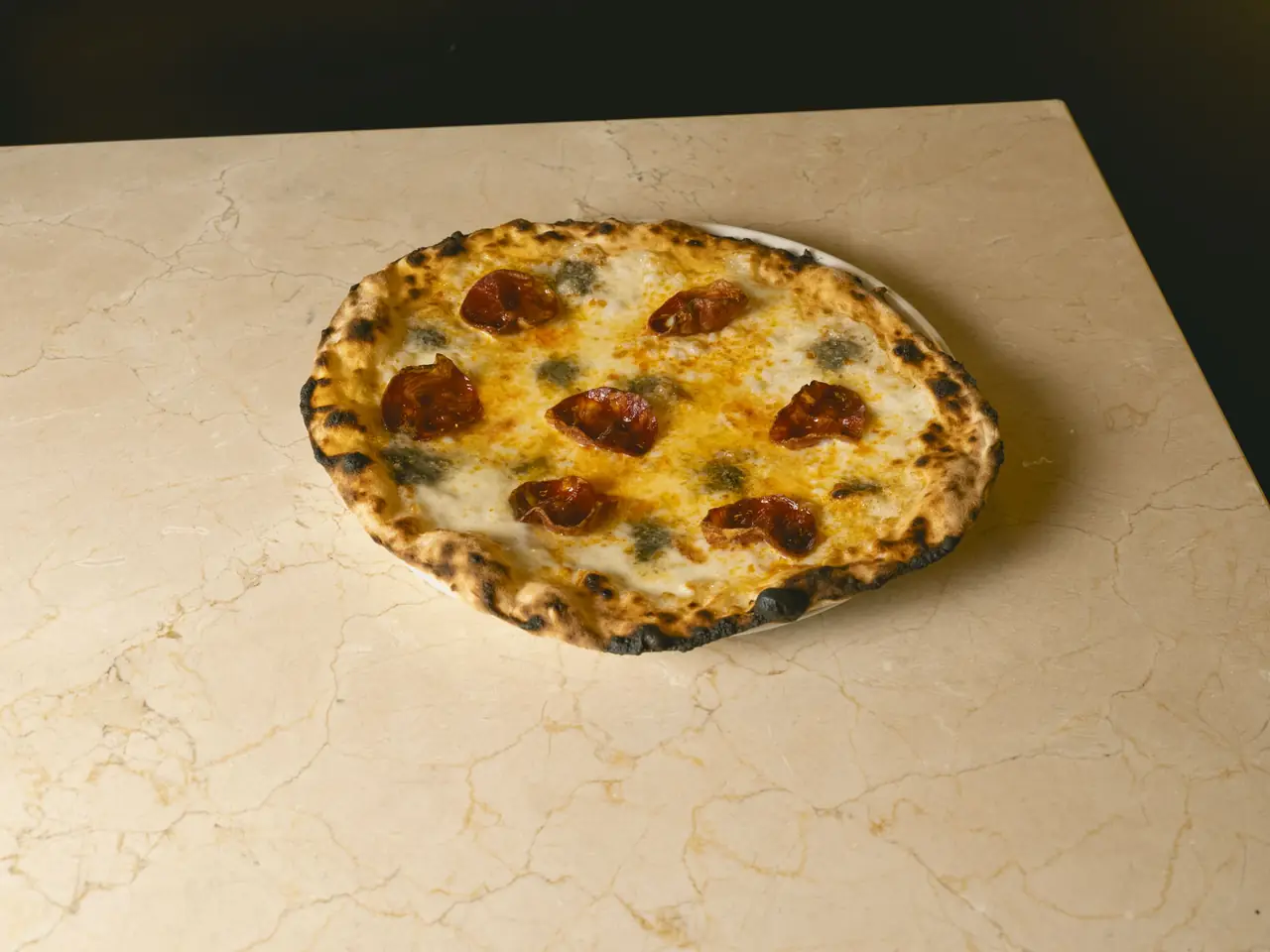 Wood-fired pizza topped with melted mozzarella, gorgonzola, and roasted cherry tomatoes on a charred, blistered crust, Romo