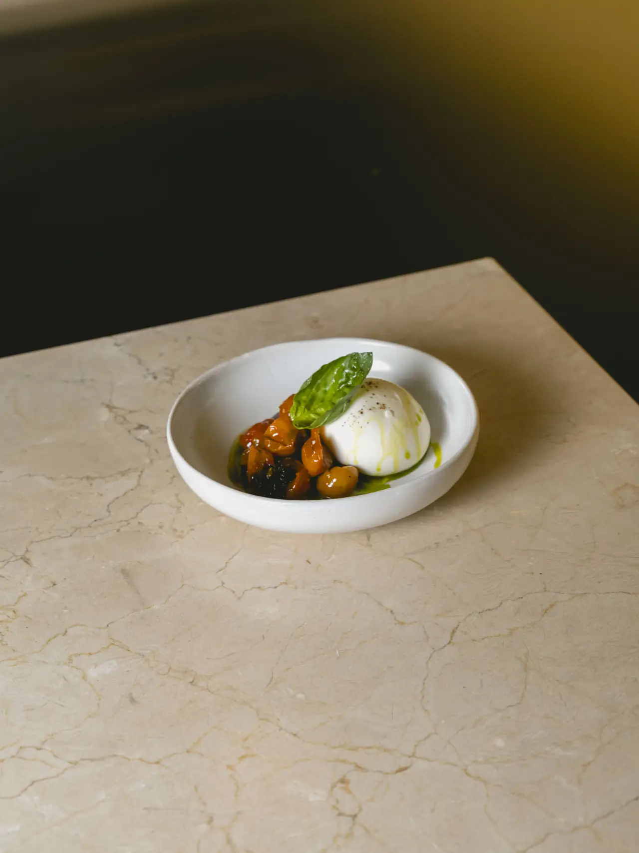 Whole burrata with a basil leaf on top, served over a citrus and dark fruit compote drizzled with green oil, Romo