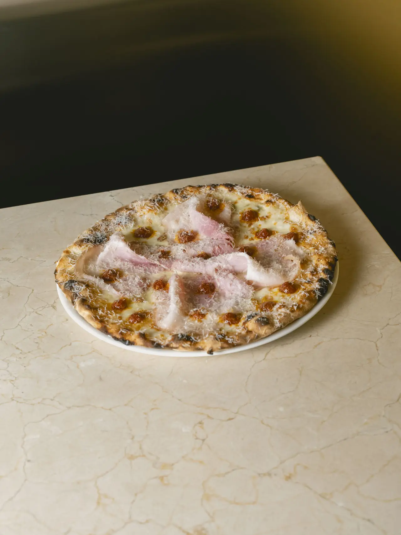 Wood-fired pizza topped with melted cheese, tomato sauce dots, and folded slices of cured ham, finished with grated cheese, Romo