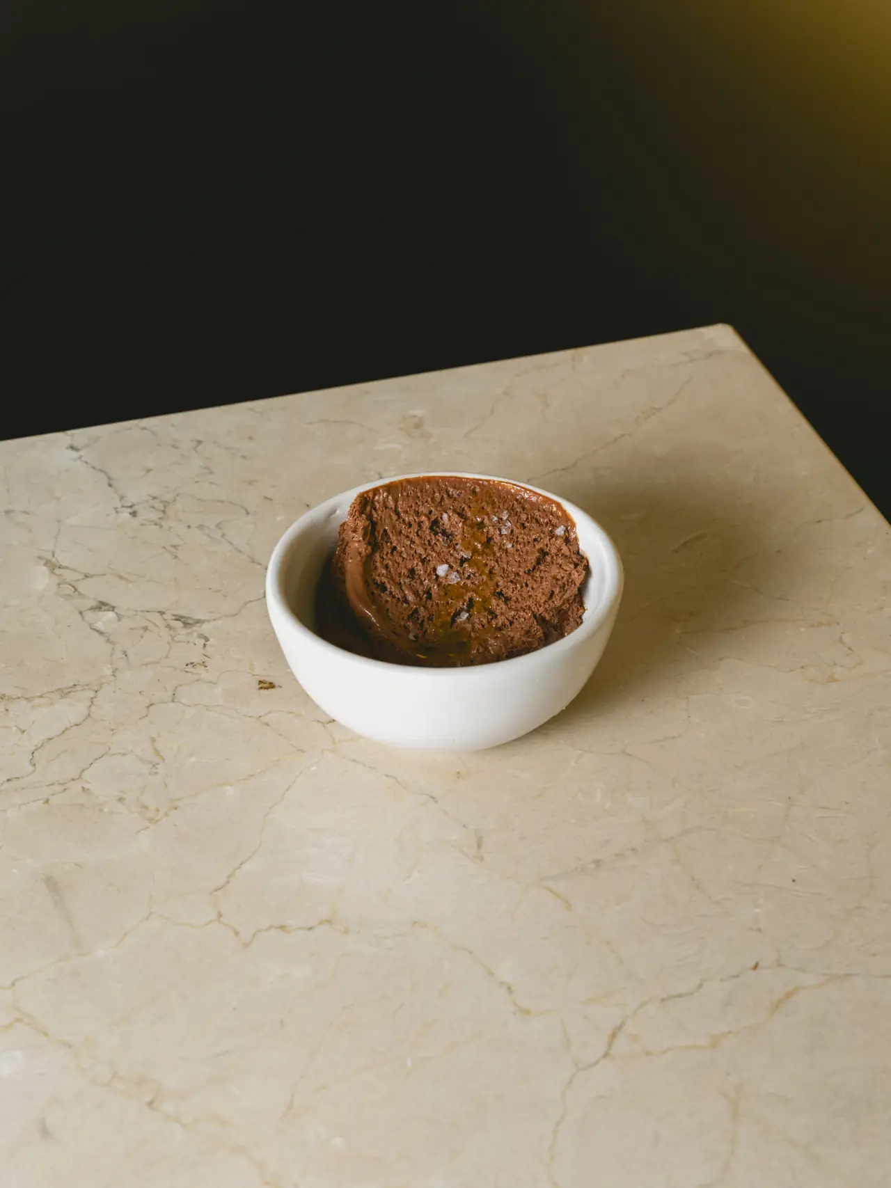 Chocolate mousse in a small white bowl, drizzled with oil and finished with flaky salt, Romo