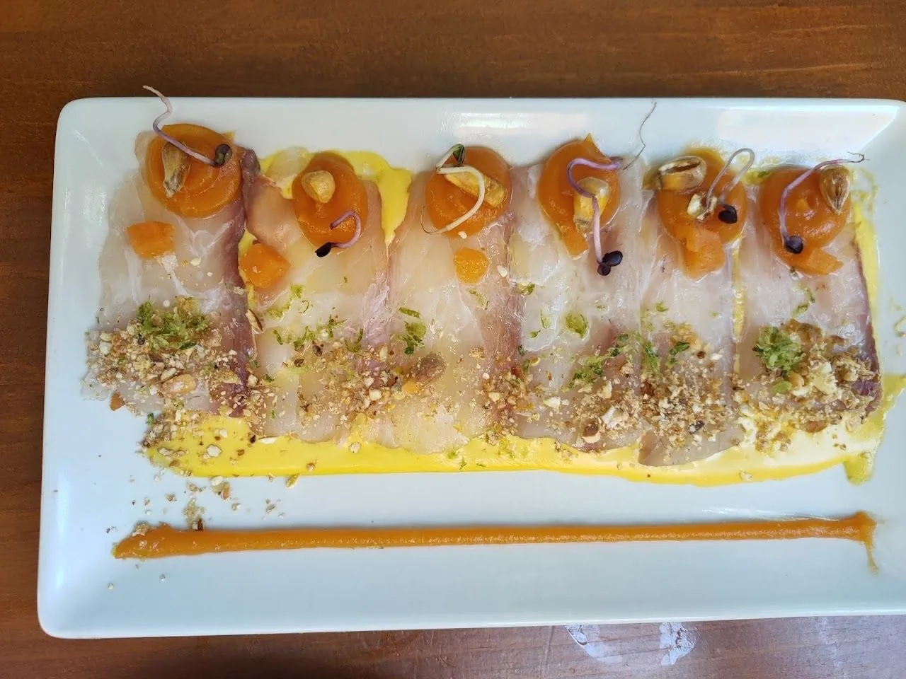 Slices of raw white fish topped with orange garnish and crumbs on a rectangular white plate