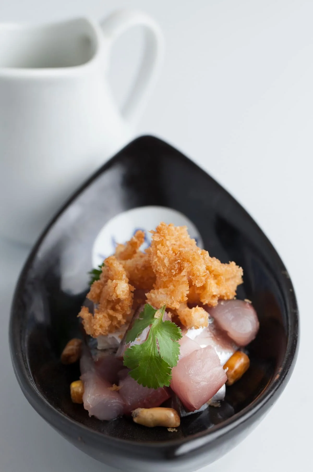 Pieces of raw fish topped with a crisp golden garnish and a green leaf in a black teardrop-shaped dish