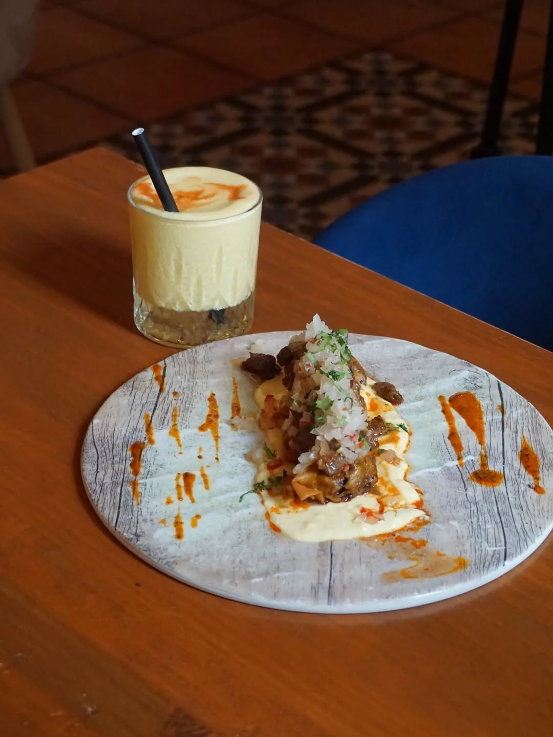 A plate of diced raw fish on rice with orange sauce next to a small glass with a creamy drink