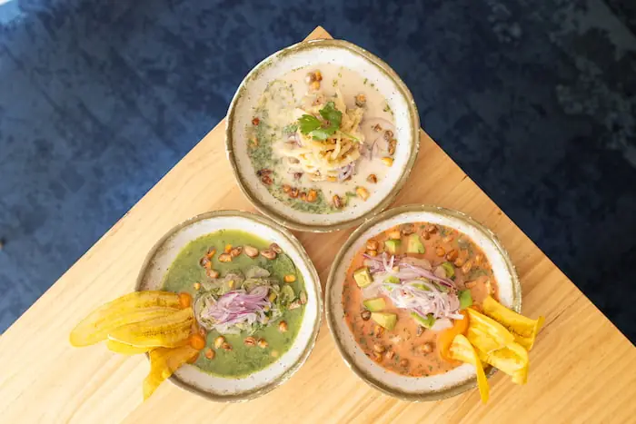 Three bowls of Peruvian ceviche with plantain chips on a wooden board