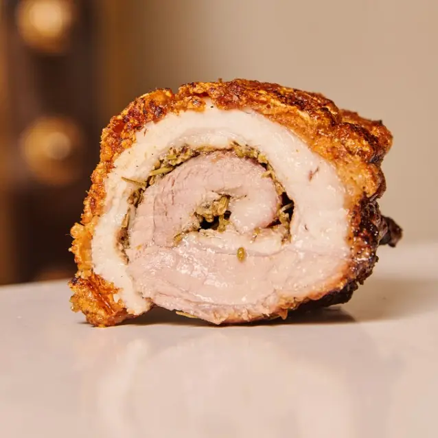 Cross-section of a rolled, herb-stuffed roast pork porchetta showing crisp browned skin and layered meat, at Rooster & Bubbles