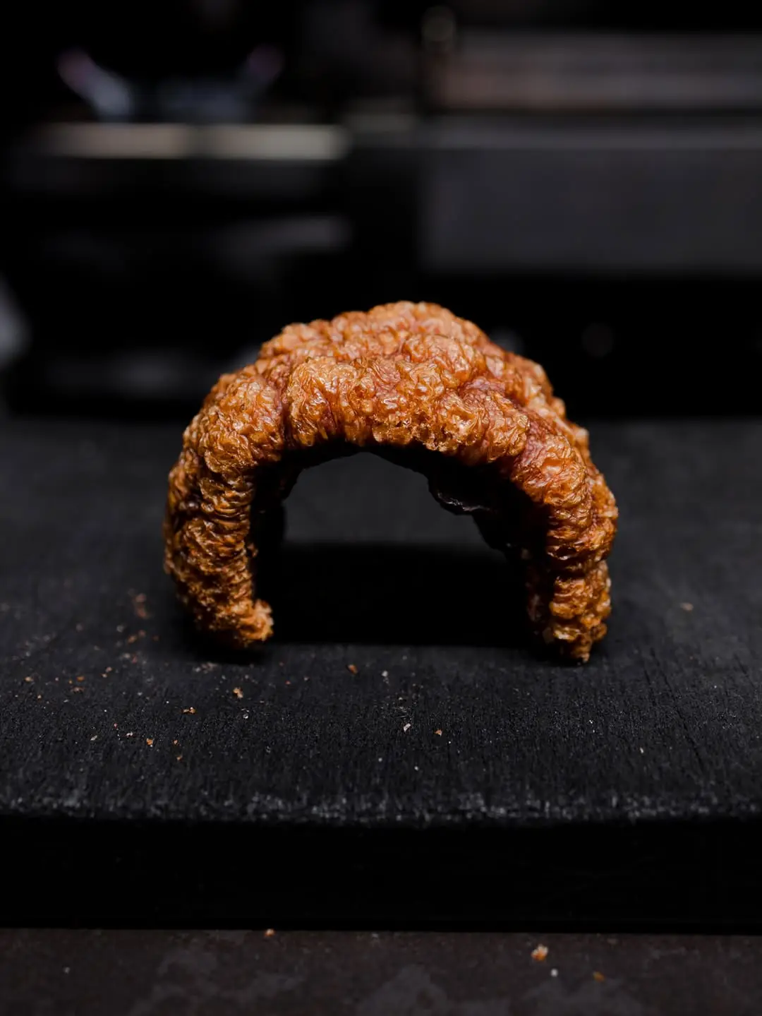 A crescent-shaped piece of crispy-skinned roasted pork belly on a dark surface