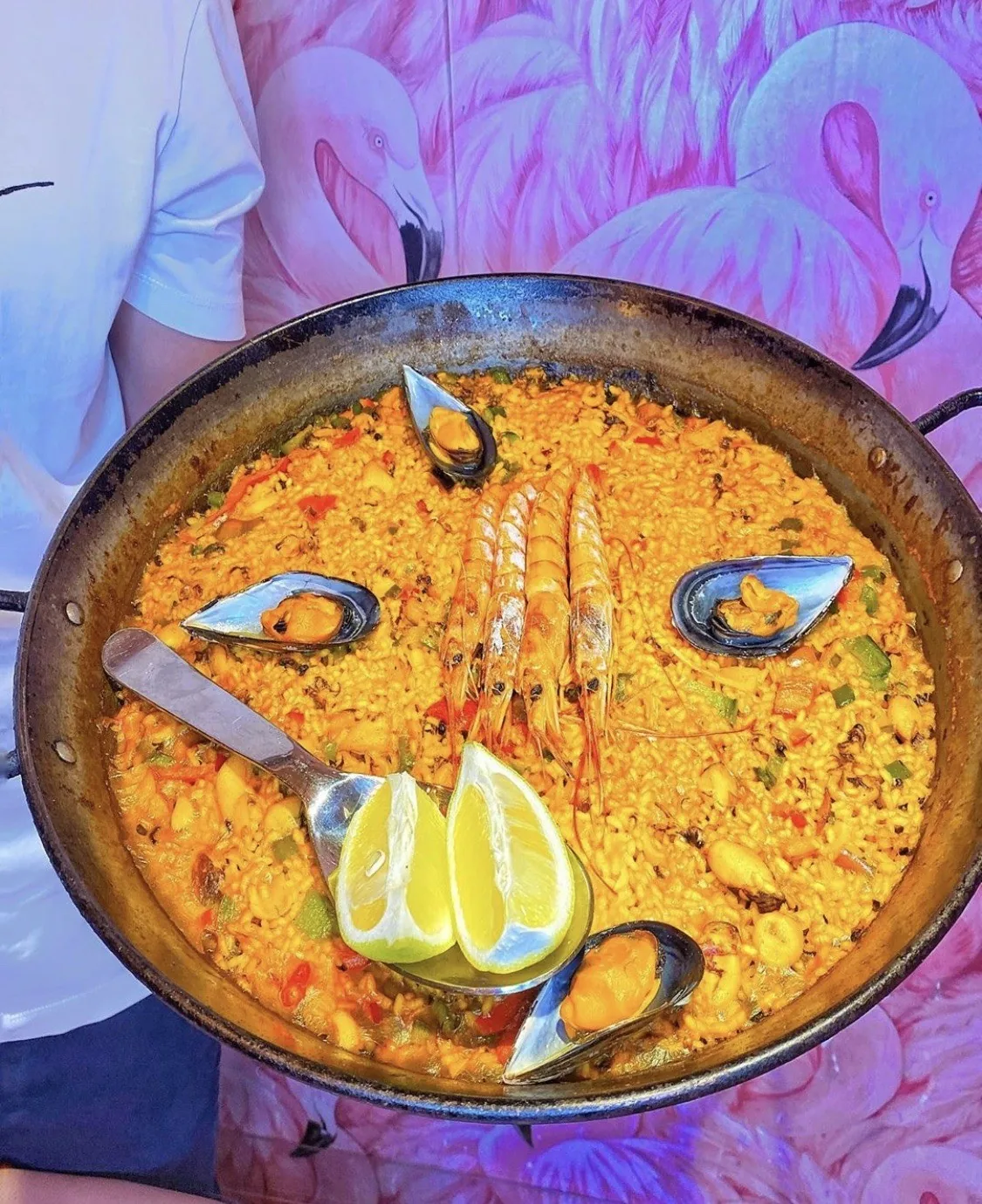 A paella pan of orange rice with mussels, prawns and lemon wedges
