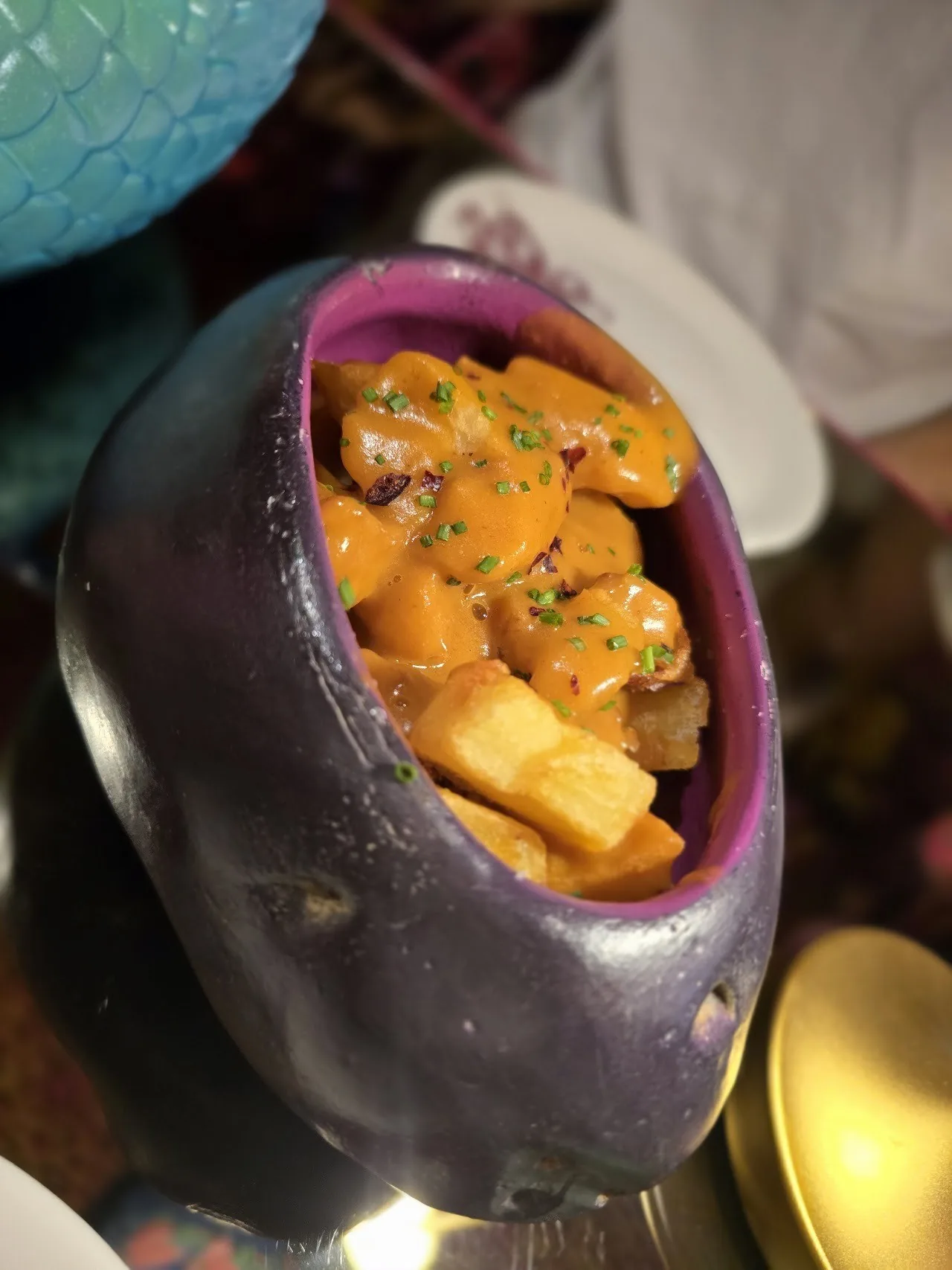 A dark bowl of fried potato pieces covered in an orange sauce with chives