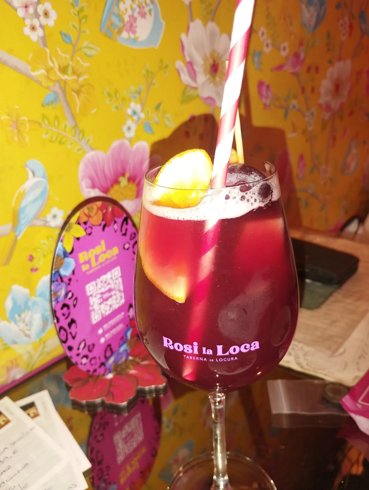 A red cocktail being poured into a glass with a lemon twist