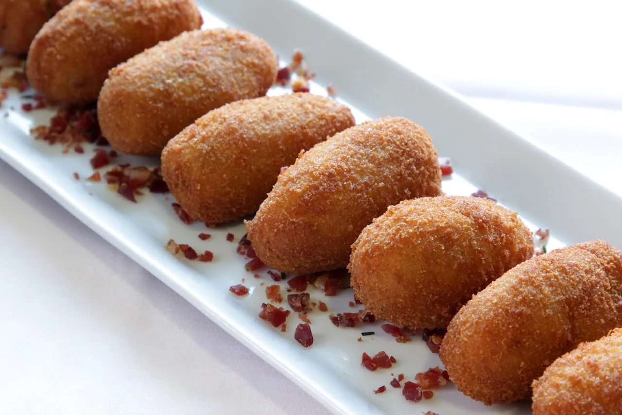 A row of breaded croquettes with a spicy garnish