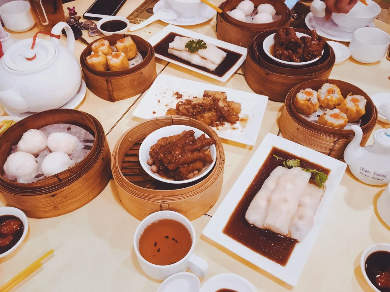A table covered with bamboo steamers of dim sum, rice rolls and dishes of sauce