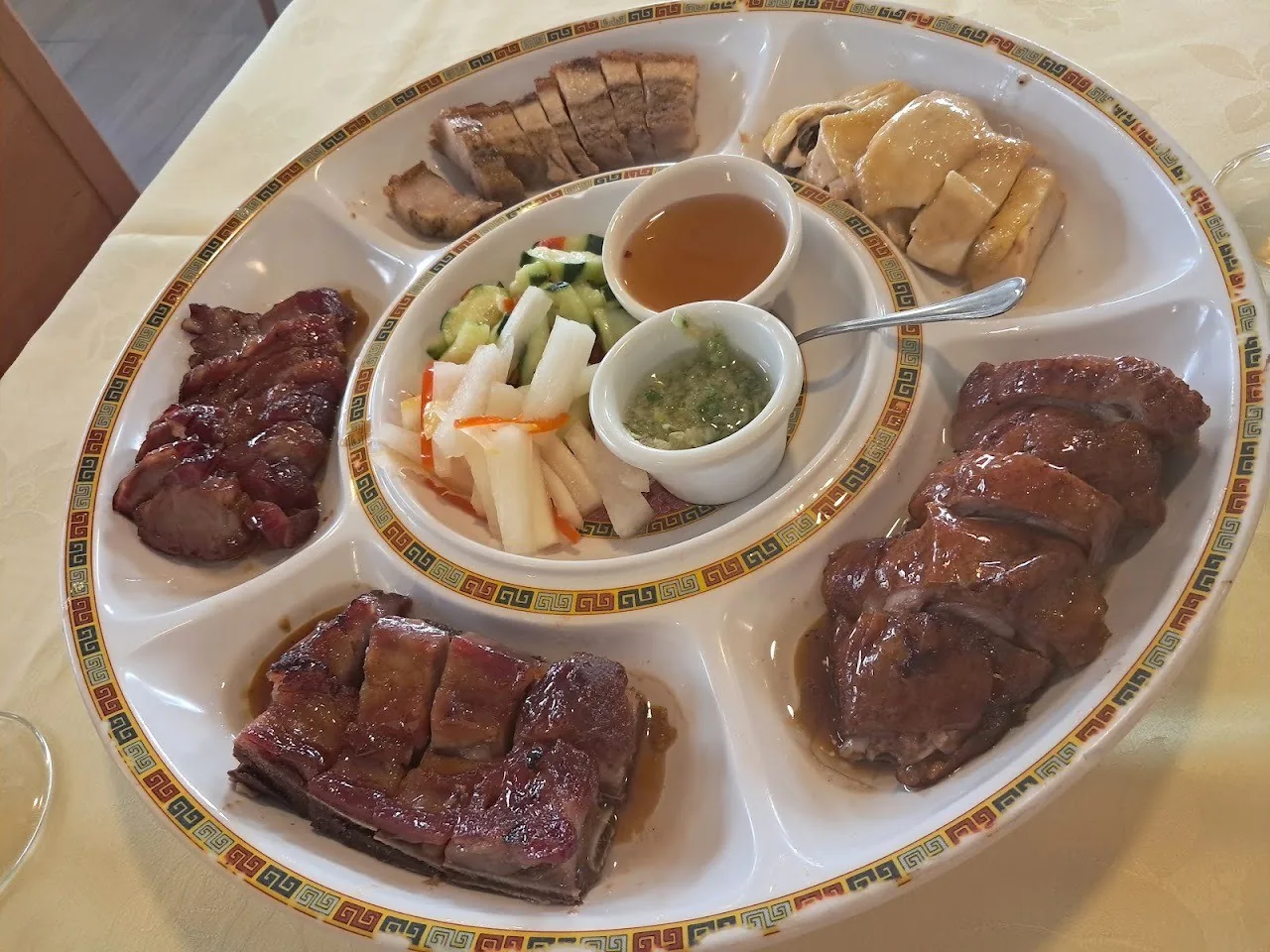 A sectioned platter of sliced roast meats with dipping sauces