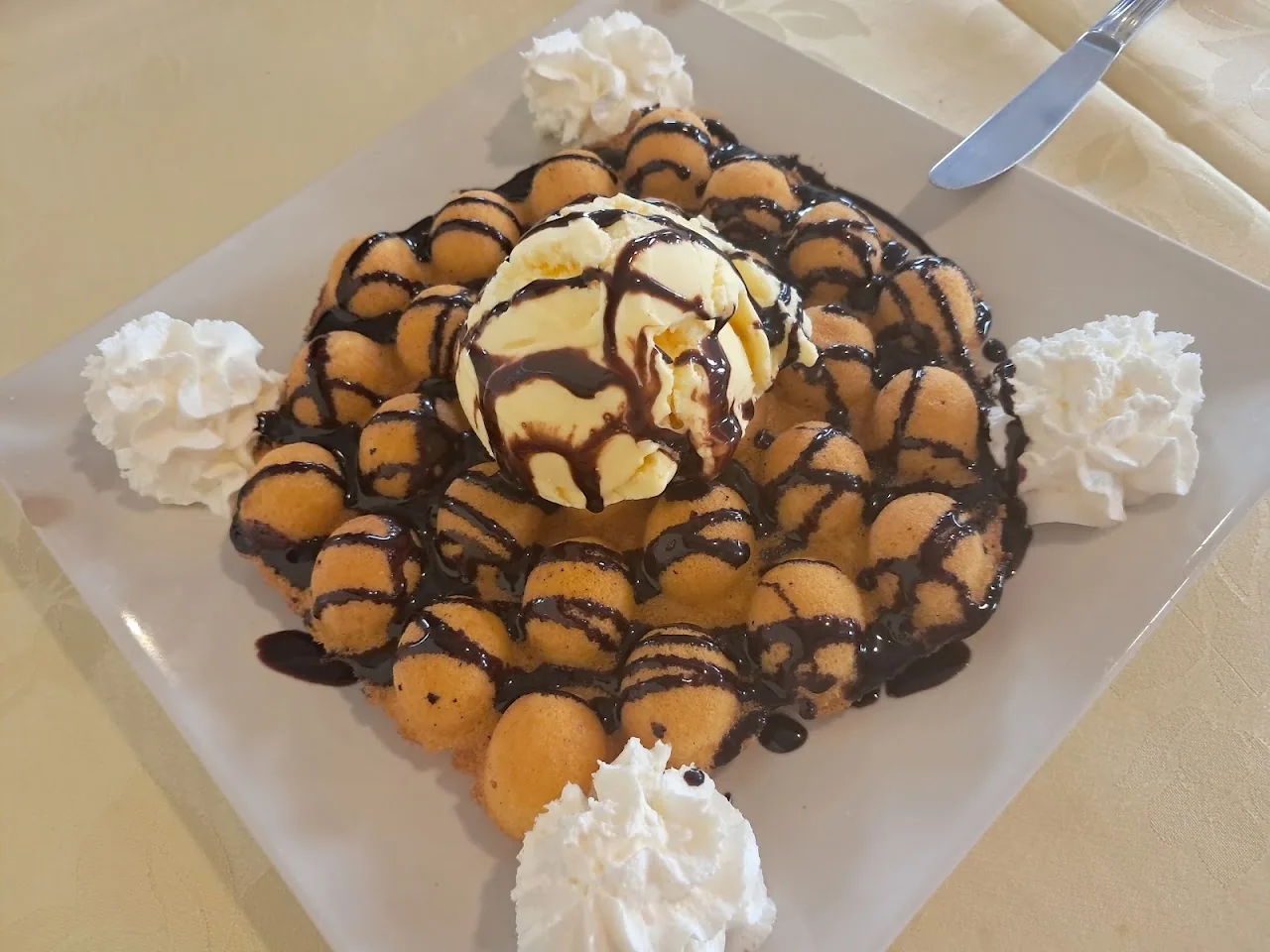 A dessert plate with a scoop of ice cream, small fried dough balls and chocolate drizzle topped with whipped cream