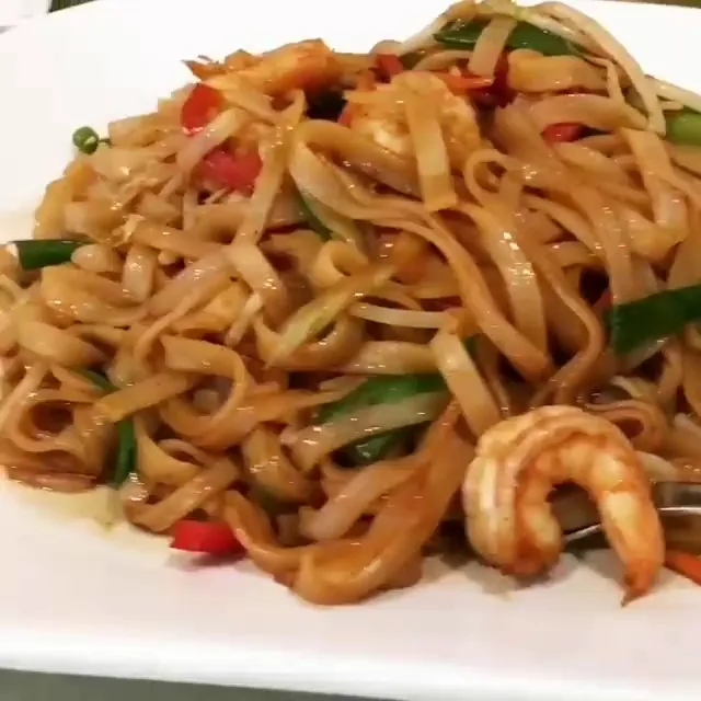 A plate of stir-fried wide noodles with shrimp, bell peppers and vegetables