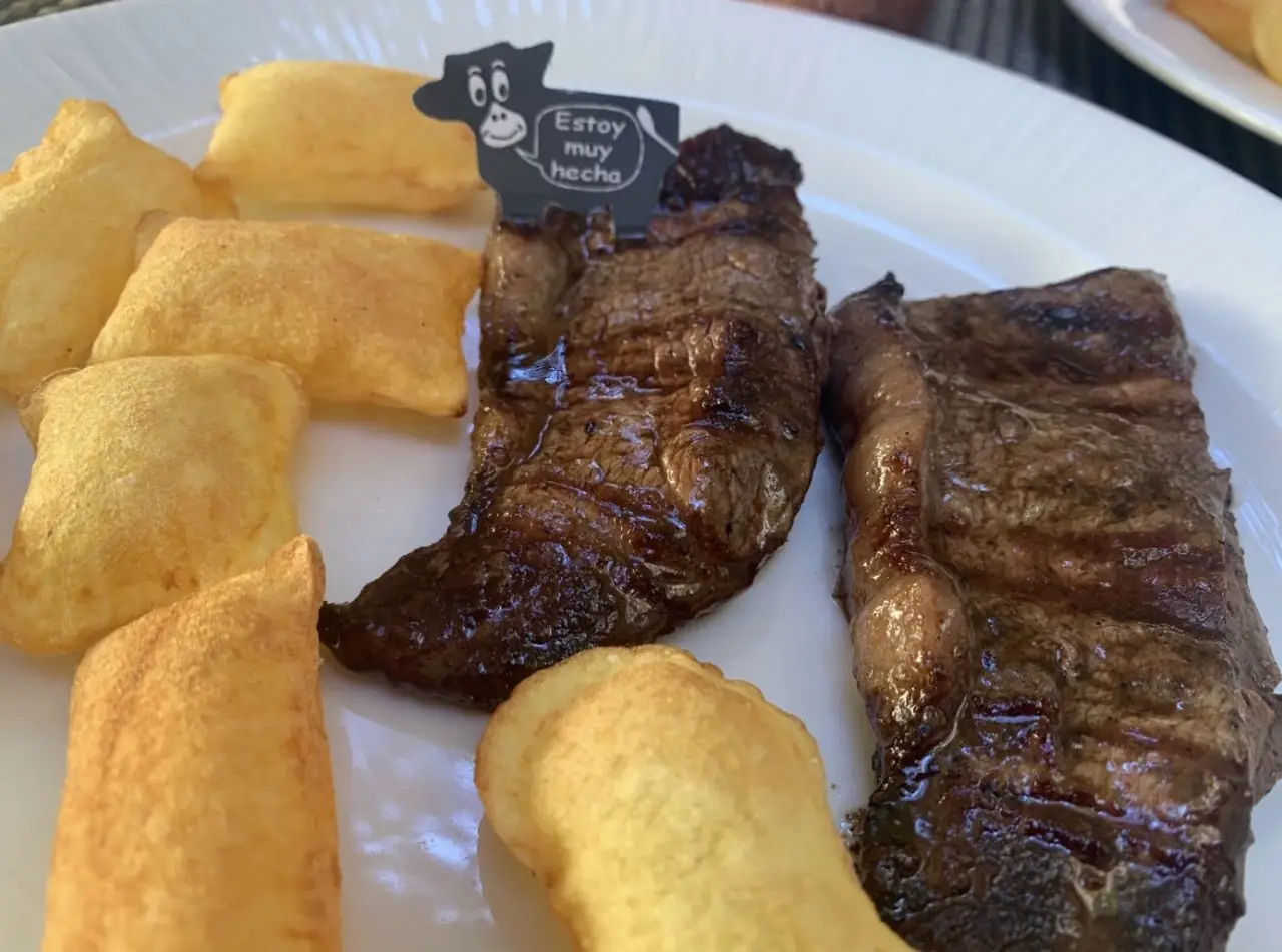 Grilled steak with crispy potato wedges on a white plate, doneness marker card beside it