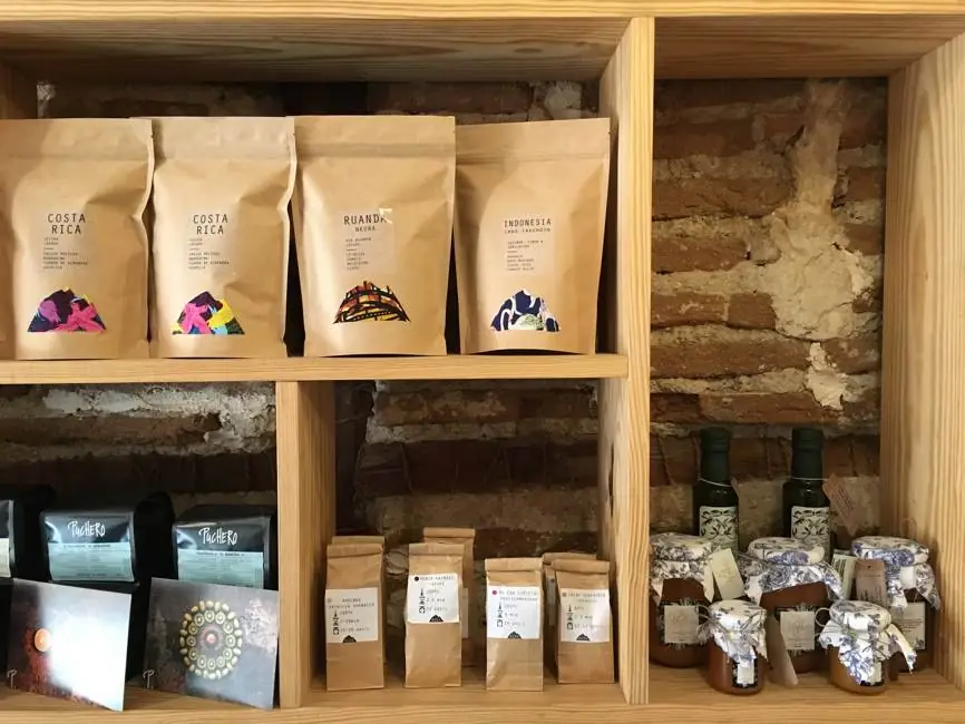 Wooden retail shelf of the cafe stocked with labelled coffee bags (Costa Rica, Ruanda, Indonesia) and jars of jam and oil against exposed brick