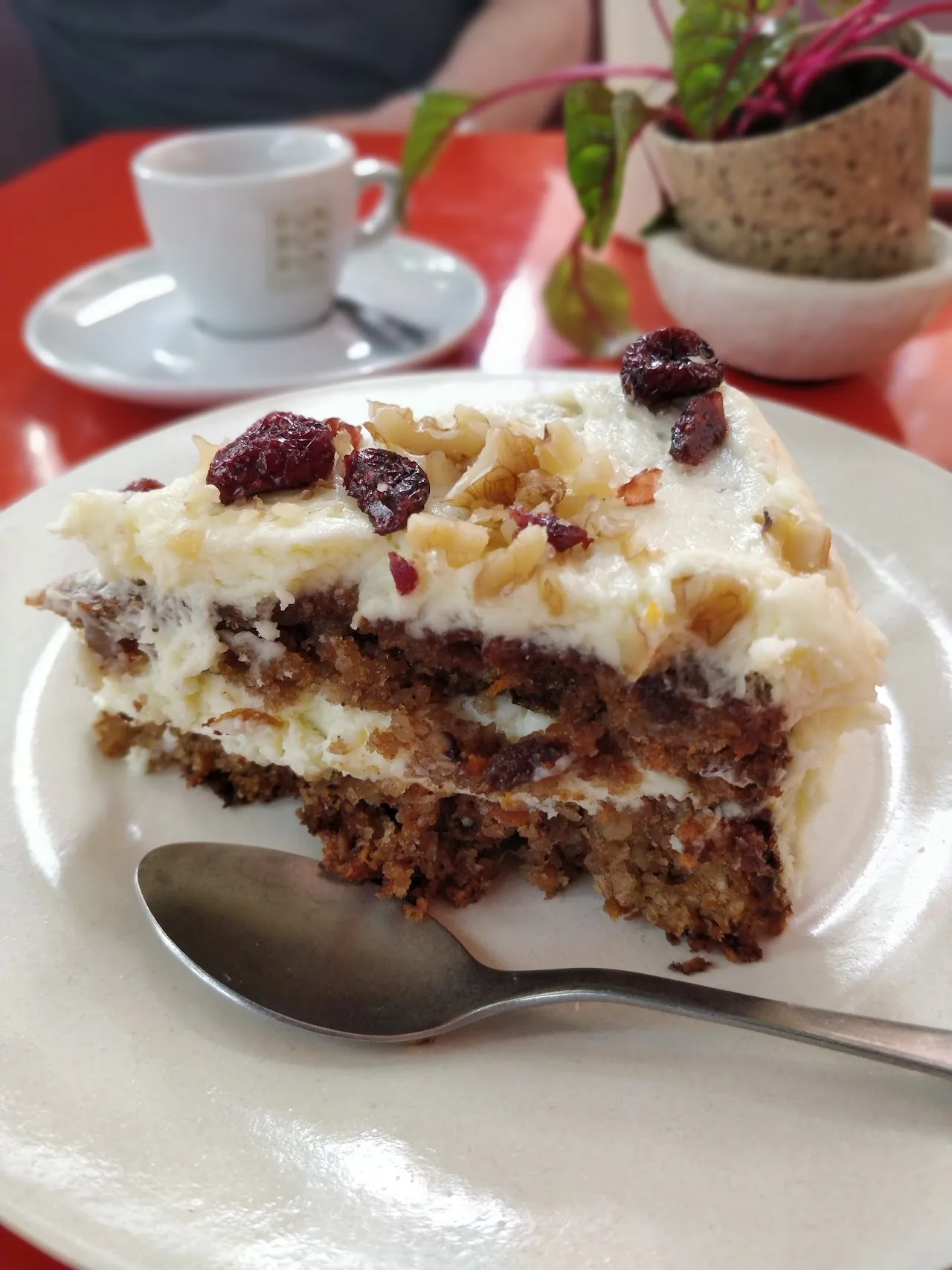 A slice of carrot cake with white frosting on a plate with a spoon