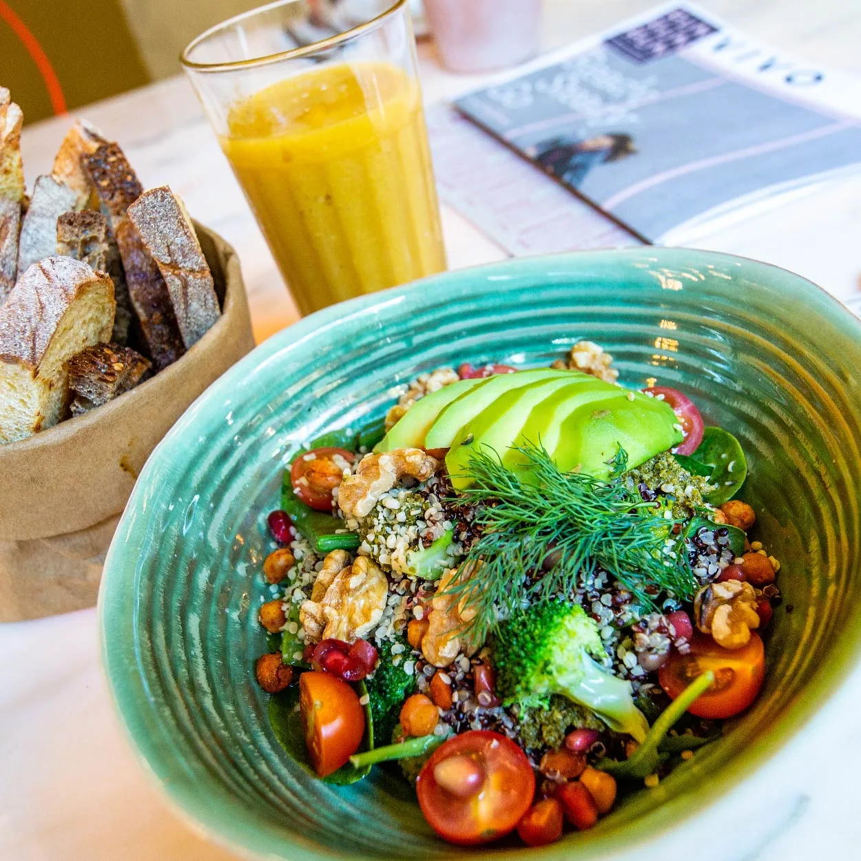 A colorful bowl with avocado slices, mixed greens, tomatoes, seeds and citrus