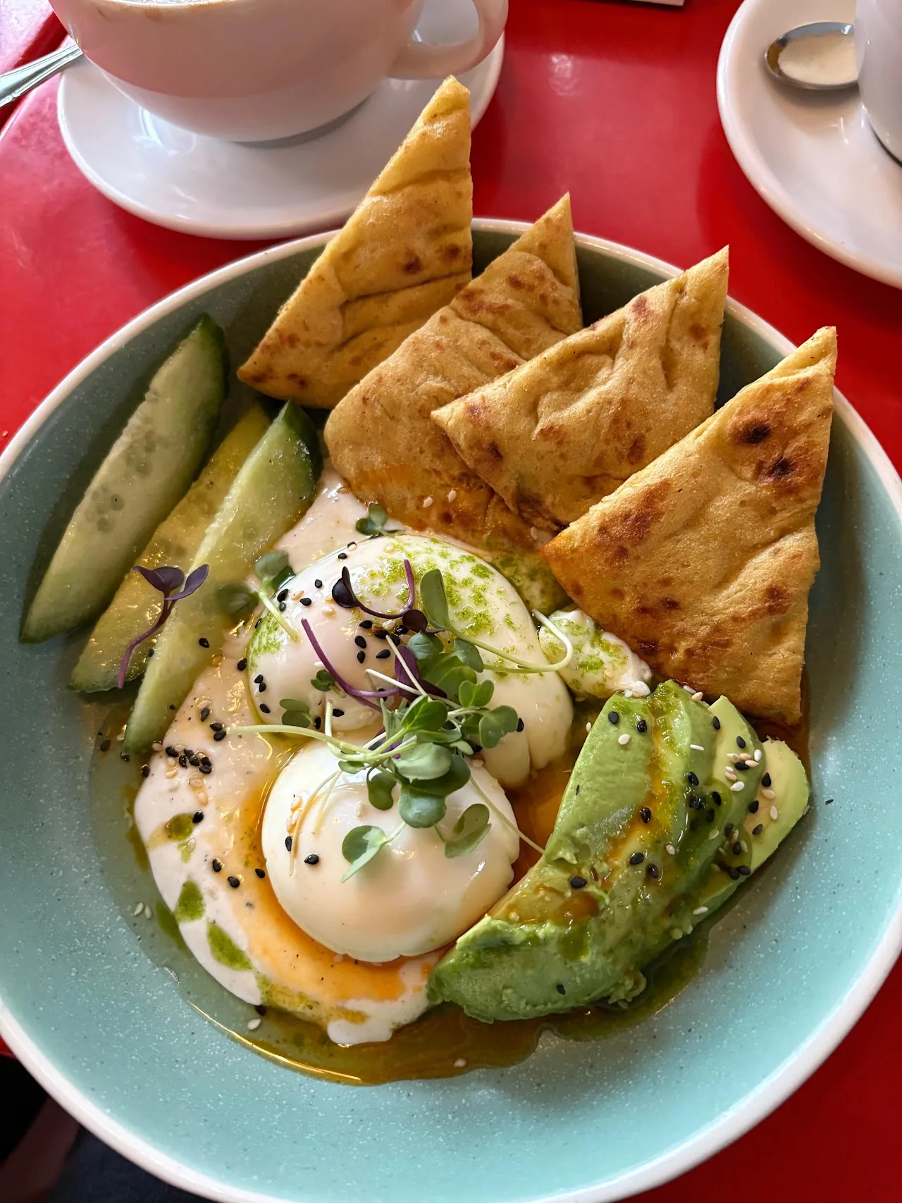 A bowl with poached eggs, avocado, cucumber slices and toasted pita wedges